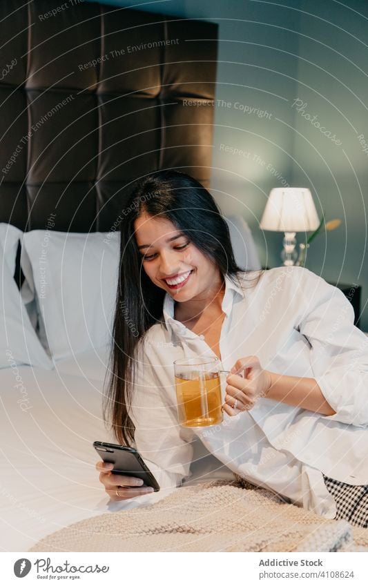 Frau trinkt Tee und telefoniert in einem Hotelzimmer Smartphone benutzend Bett positiv Glück sich[Akk] entspannen trinken gemütlich Becher ruhen heimwärts