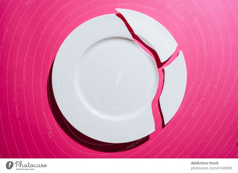 Zerbrochener weißer Teller auf rosa Hintergrund gebrochen Riss Geschirr erdrücken Bruchstück Scherbe Spielfigur Porzellan Keramik Holzplatte Sauberkeit leer