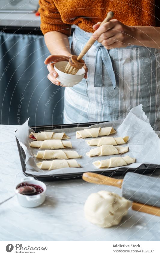 Koch hält Schüssel und streicht Croissants in Backblech auf Tisch Marmelade Teigwaren rollierend Nudelholz Vorbereitung aufgeschnitten Bäckerei selbstgemacht