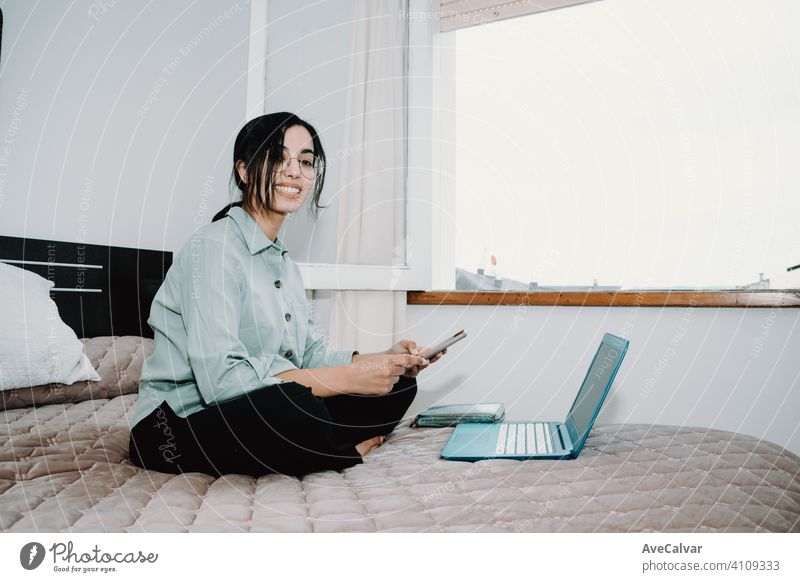 Junge arabische Frau arbeitet zu Hause auf seinem Laptop, während mit seinem Telefon über seinem Bett mit Kopie Raum Technik & Technologie heimwärts Sitzen