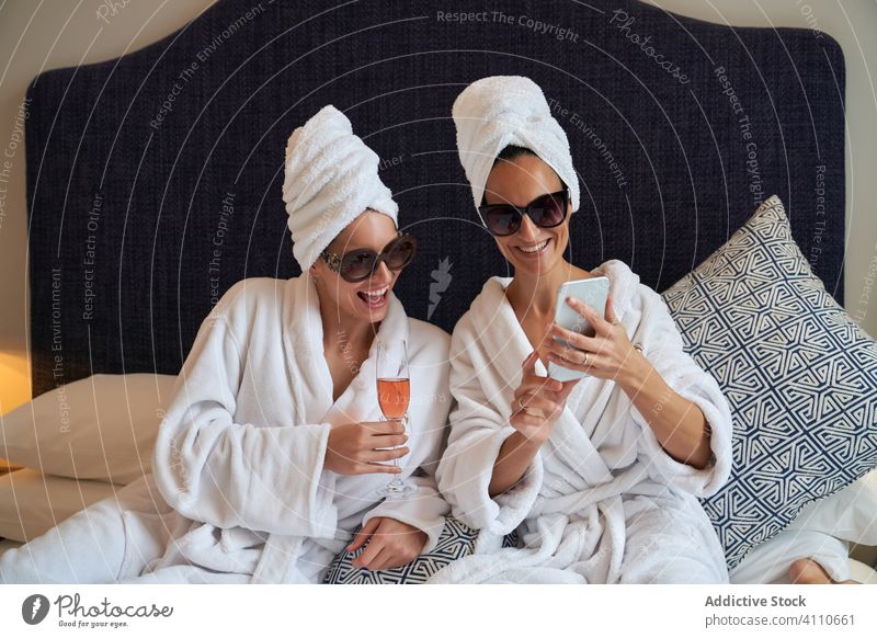 Freunde benutzen ihr Smartphone, während sie sich auf einer Pyjamaparty im Schlafzimmer entspannen Fotografie Getränk feiern Lächeln Glück Bademantel Bett
