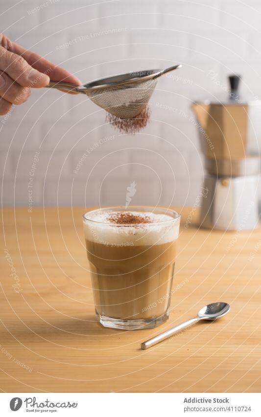 Gesichtsloser Barkeeper, der seinen Kaffee mit Kakaopulver garniert vorbereiten Dienst Glas Latte Cappuccino Sieb schäumen Pulver frisch brauen melken Café