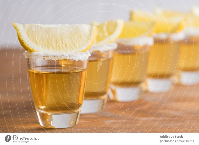 Schuss Alkohol mit Zitronenscheiben oben drauf Tequila Scheibe Spielfigur Schnaps Reihe Glas Tisch hölzern Wand trinken Getränk Erfrischung geschmackvoll kalt
