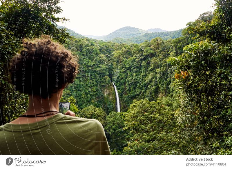 Anonymer Reisender mit Smartphone in der Nähe eines Wasserfalls Mann benutzend Dschungel üppig (Wuchs) reisen grün Natur Costa Rica männlich Ausflug erkunden
