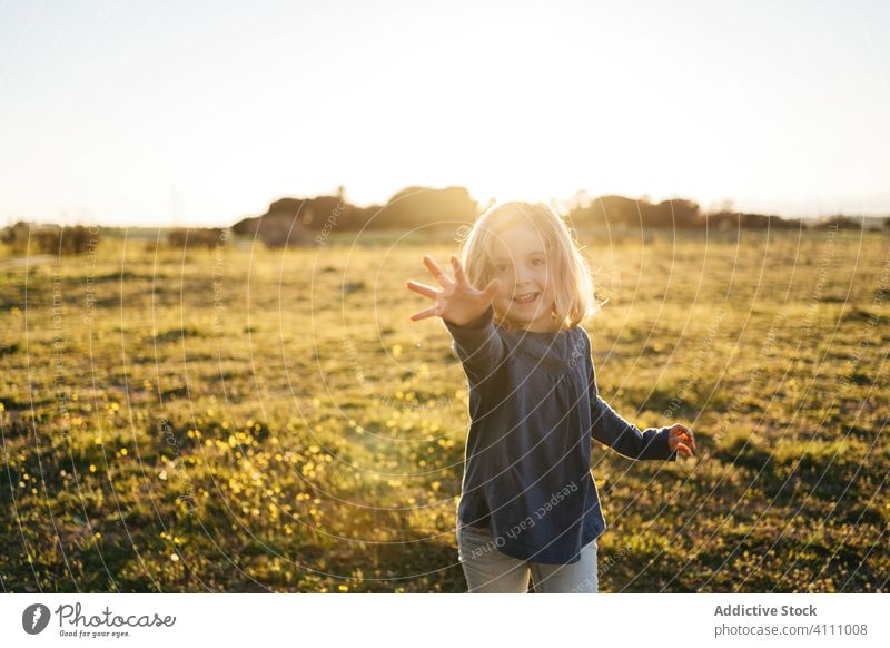 Fröhliches kleines Mädchen auf einem Feld im Sommerabend Kind Glück Natur genießen Spaß haben Sonnenuntergang Abend Lächeln spielerisch ausdehnen gestikulieren