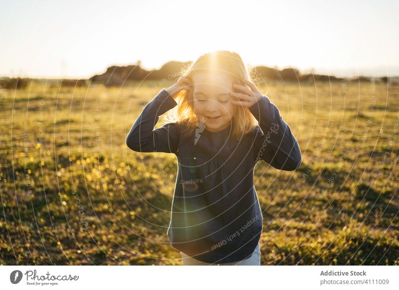 Fröhliches kleines Mädchen auf einem Feld im Sommerabend Kind Glück Natur genießen Spaß haben Sonnenuntergang Abend Lächeln spielerisch ausdehnen gestikulieren