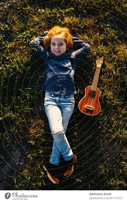 Kleines Mädchen liegt mit Ukulele im Gras Kind spielen Musik Gitarre Natur Baum Sommer wenig Instrument Klang Gesang Melodie Kofferraum ausführen üben ruhen
