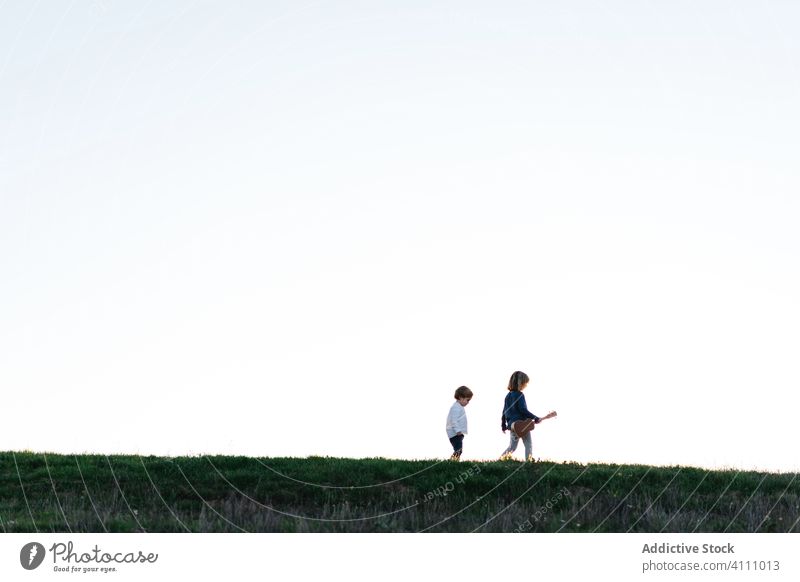 Kleine Schwester und Bruder gehen im Feld Kinder Natur Sommer Spaziergang Sonnenuntergang Abend Zusammensein erkunden Gras Ukulele Gitarre folgen