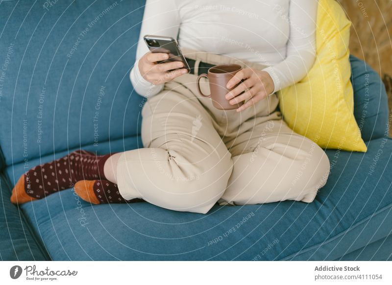 Crop Geschäftsfrau ruht auf Couch mit Kaffee und Telefon Pause ruhen Liege Smartphone Kälte benutzend Komfort sich[Akk] entspannen Apparatur Sofa Browsen
