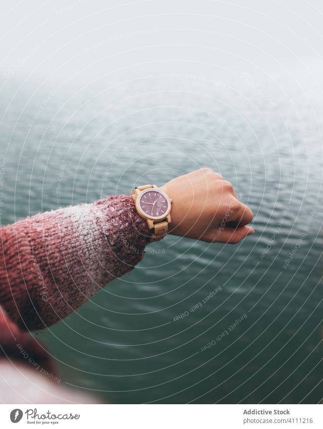 Frau, die am Fluss steht und die Zeit auf ihrer Armbanduhr überprüft zuschauen Stil trendy Wasser aktiv Landschaft Hand Natur Saison weiß kalt Mode Outfit