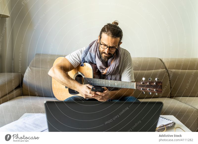 Junger männlicher Musiker beim Surfen auf dem Smartphone im Wohnzimmer Browsen zuschauend reden Anruf Gitarre benutzend Laptop sitzen Liege Songwriter Komponist