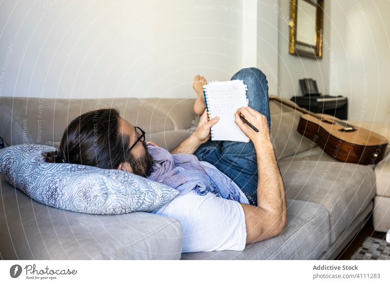 Mann schreibt Notizen auf Couch in gemütlichem Wohnzimmer Liege schreiben Hinweis Sofa männlich lässig Komfort Songwriter Lügen Dichter Komponist