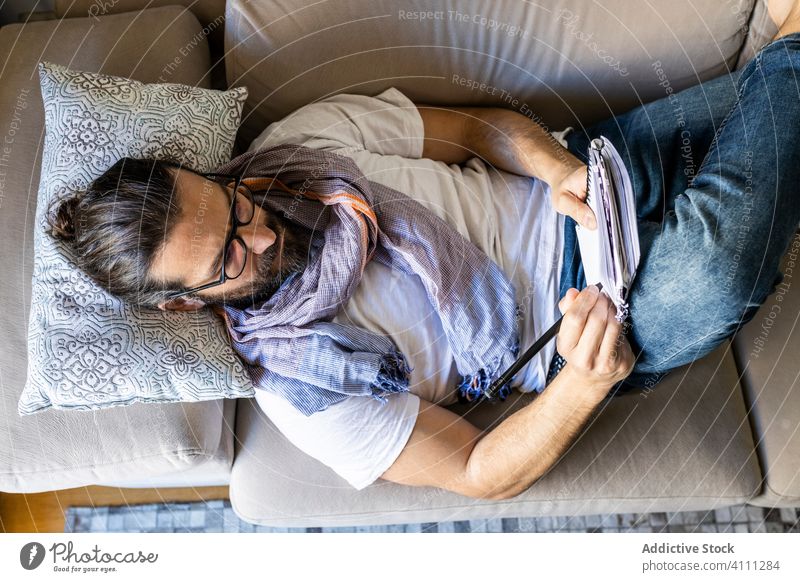 Mann schreibt Notizen auf Couch in gemütlichem Wohnzimmer Liege schreiben Hinweis Sofa männlich lässig Komfort Songwriter Lügen Dichter Komponist