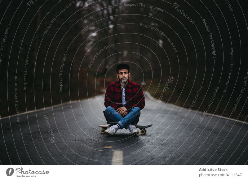 Junger Mann auf der Straße mit Skateboard in der Landschaft ruhend sitzen Lifestyle männlich lässig jung Natur Asphalt sich[Akk] entspannen Wald cool Freiheit