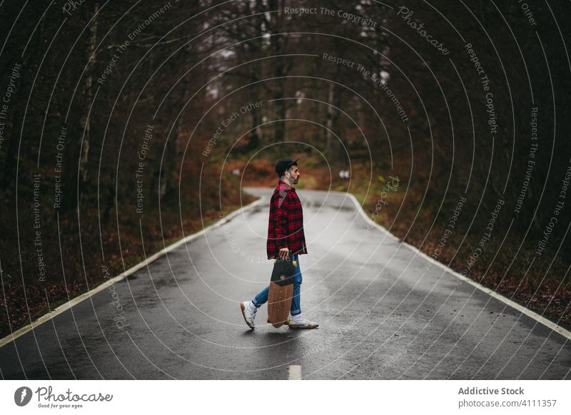 Männlicher Skater auf der Straße im Herbstwald Mann Wald Skateboard Landschaft lässig Spaziergang Stil männlich Baum leer Asphalt Natur Freiheit Abenteuer