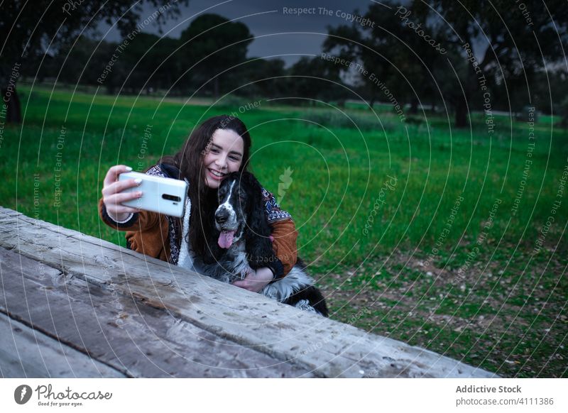 Zufriedene Dame, die mit ihrem Smartphone ein Selfie mit ihrem Hund im Park macht Frau Lächeln Lachen genießen Mobile Telefon Spaniel Umarmung Umarmen Tier