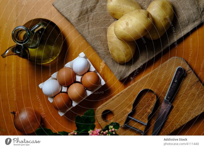 Zutaten und Werkzeuge für das Rezept auf dem Tisch Kartoffel Ei Erdöl Bestandteil vorbereiten oliv Zwiebel Messer sich[Akk] schälen Küche hölzern Lebensmittel