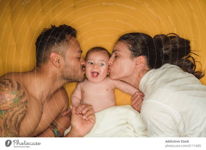 Mutter und Vater küssen ihr Baby Kuss Zusammensein Umarmung Familie Umarmen Liebe Lügen Bett Glück Kind bezaubernd niedlich wenig Pflege Eltern