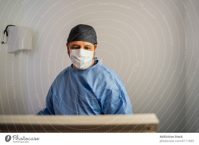 Arzt, der Informationen auf dem Bildschirm überprüft, während er eine diagnostische Patientenerkrankung in einer modernen Klinik durchführt Uniform Krankenhaus