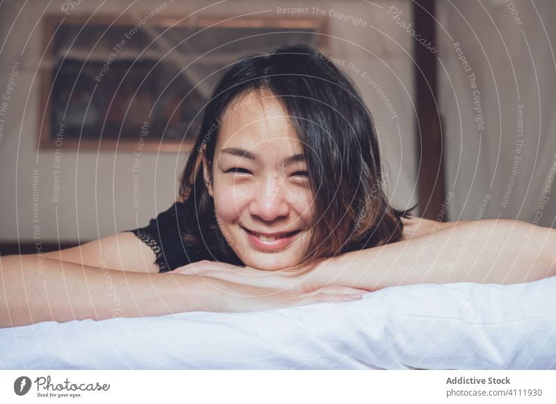Glückliche ethnische Frau auf dem Bett liegend Lügen heimwärts Lachen Morgen sich[Akk] entspannen Schlafzimmer Komfort ruhen Wochenende heiter gemütlich