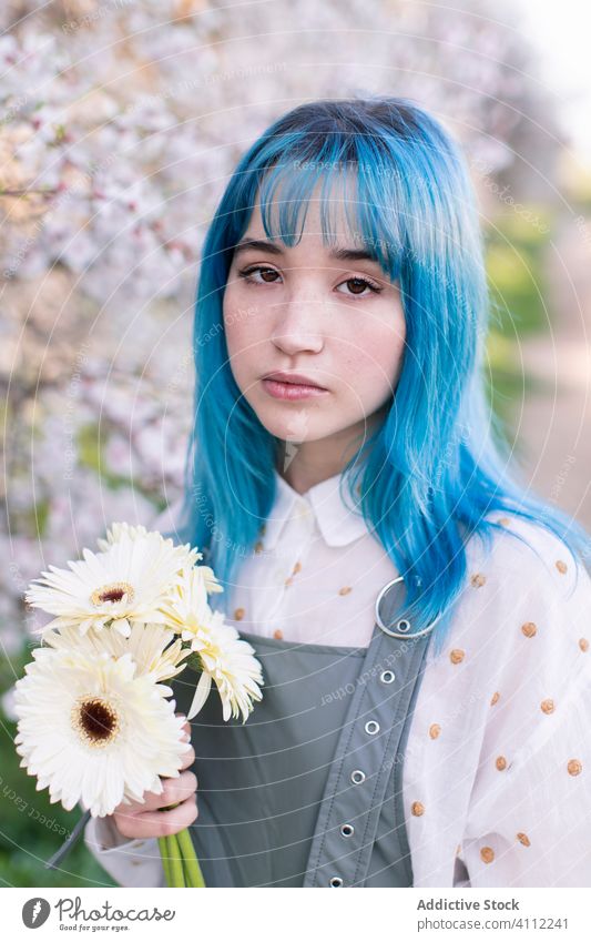 Stilvolle junge Frau mit Blumen in einem blühenden Garten stehend Frühling Blütezeit Melancholie informell alternativ trendy blaue Haare modern gefärbtes Haar
