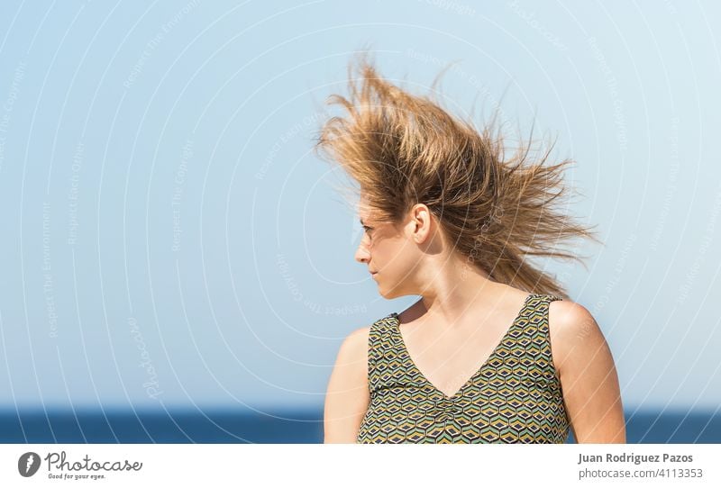 Porträt einer blonden kaukasischen Frau mittleren Alters in einem grünen Kleid und mit im Wind schüttelnden Haaren MEER Sommer Sonne sich[Akk] entspannen