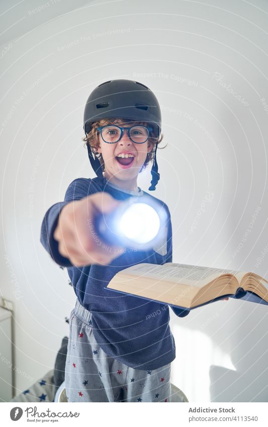 blondes Kind im Schlafanzug mit einem Helm, einer Taschenlampe und einem Buch, das Forschung spielt Kinder Schutzhelm Spiel behüten Fröhlichkeit Genuss spielen