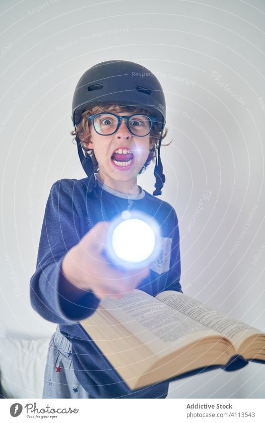 blondes Kind im Schlafanzug mit einem Helm, einer Taschenlampe und einem Buch, das Forschung spielt Kinder Schutzhelm Spiel behüten Fröhlichkeit Genuss spielen