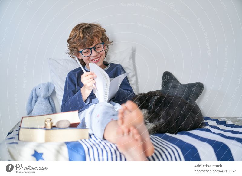 blonder Junge mit Brille schreibt in ein Notizbuch Kinder Teenager Hausaufgabe lernen Hinweis Schreibstift lesen schreibend Tagebuch lehrreich Ausdrücken