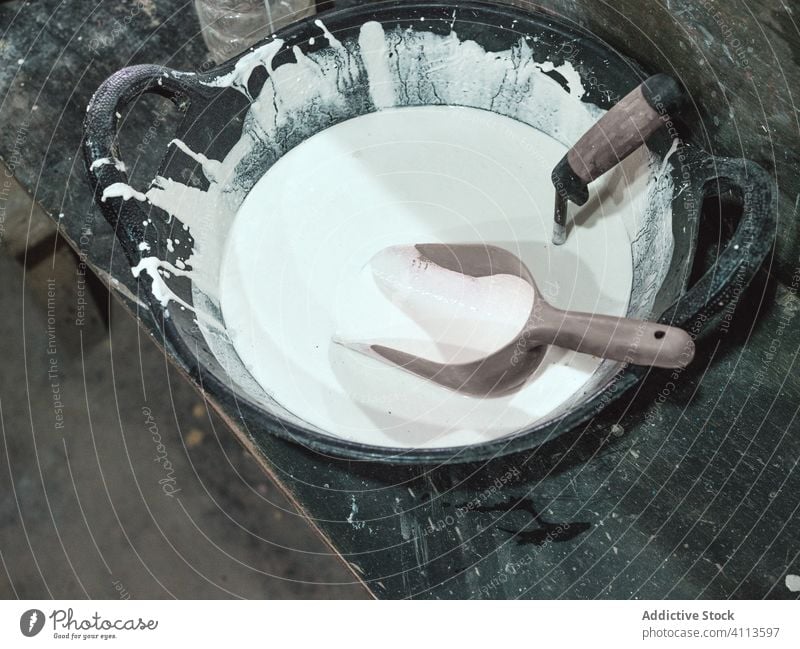 Weißes flüssiges Material mit Werkzeugen im Behälter Container Keramik liquide Herstellung Kunst Kunsthandwerk Ton Werkstatt hölzern Tisch Schreibtisch Kelle