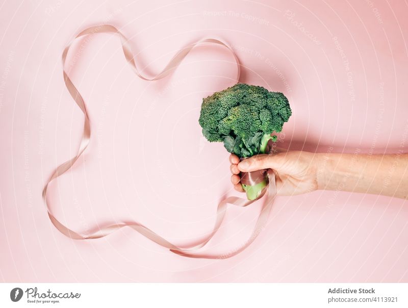 Crop Person mit gesundem Brokkoli und rosa Schleife Diät Gesundheit zeigen organisch Konzept frisch Lebensmittel Gemüse Vegetarier Vitamin Veganer Veggie grün