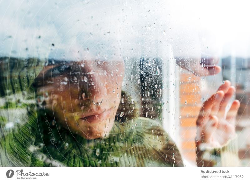 Melancholische junge Frau schaut durchs Fenster traurig Depression Isolation Coronavirus heimwärts verzweifelt einsam unglücklich männlich nass Regen