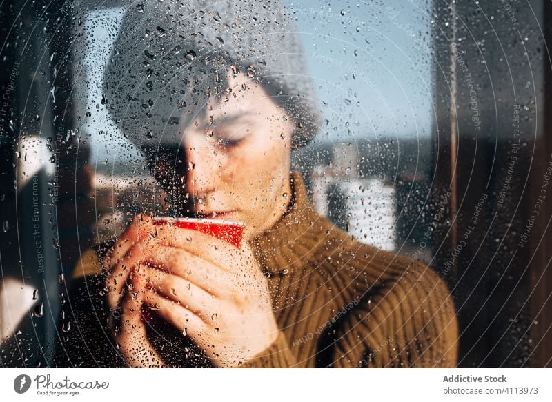 Nachdenkliche Frau trinkt Kaffee am Fenster traurig Depression trinken Selbstisolierung heimwärts unglücklich einsam COVID19 Melancholie jung nass Regen