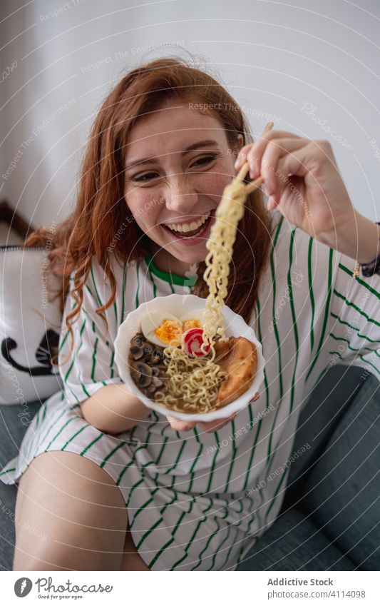 Glückliche Frau isst zu Hause Nudeln essen Ramen heimwärts Japanisch Sofa Essstäbchen jung Rotschopf heiter Lebensmittel Tradition authentisch asiatisch