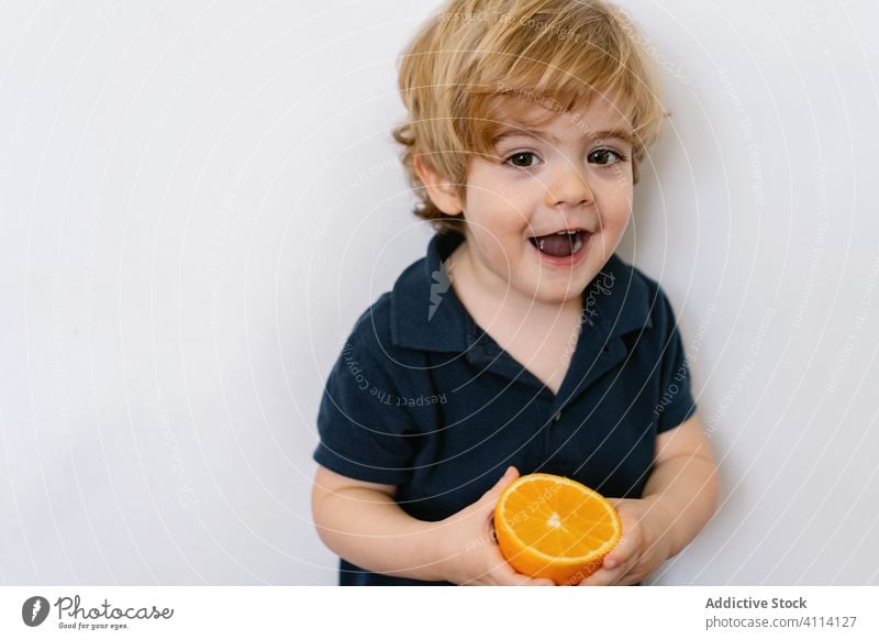 Lächelndes kleines Kind spielt mit Orangenhälfte Junge orange spielerisch Frucht charmant süß spielen Saft lustig neugierig lecker ausspannen Glück wenig heiter