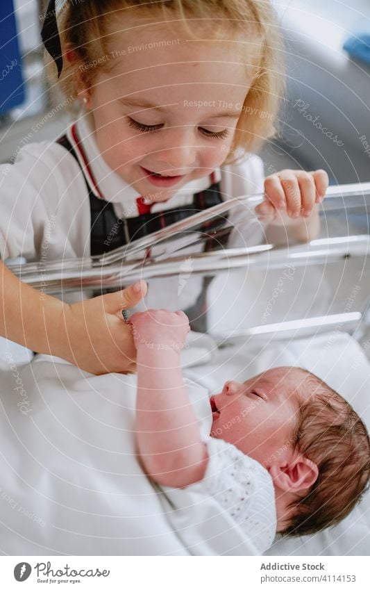 Glückliches Mädchen steht in der Nähe eines neugeborenen Geschwisters Baby Schwester Geschwisterkind schlafen Krankenhaus Babybett Wiege Kind wenig Pflege