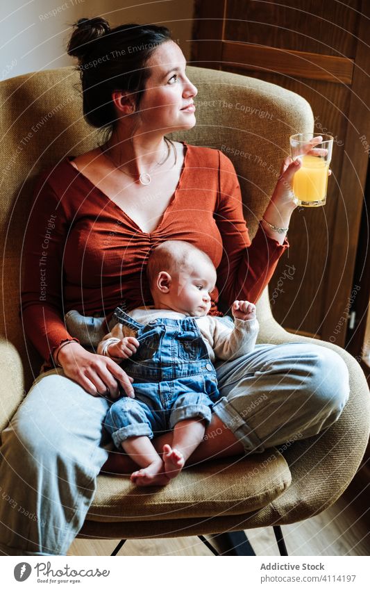 Crop-Mutter mit Saft und Baby auf einem Stuhl liegend ruhen orange Gesundheit gemütlich sitzen Liebe heimwärts Angebot Frau frisch trinken Getränk bezaubernd