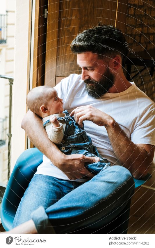 Bärtiger Vater kommuniziert mit Baby Kommunizieren Umarmung heimwärts Liebe Angebot Fenster sitzen gemütlich Stuhl Mann Säugling Kind wenig Umarmen Eltern