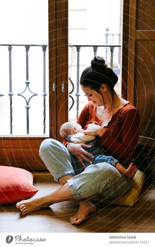Glückliche Mutter stillt Baby am Fenster Stillen Futter Brust heimwärts Liebe ruhen gemütlich sitzen Frau niedlich Raum Umarmung Umarmen Lächeln Kind Kindheit