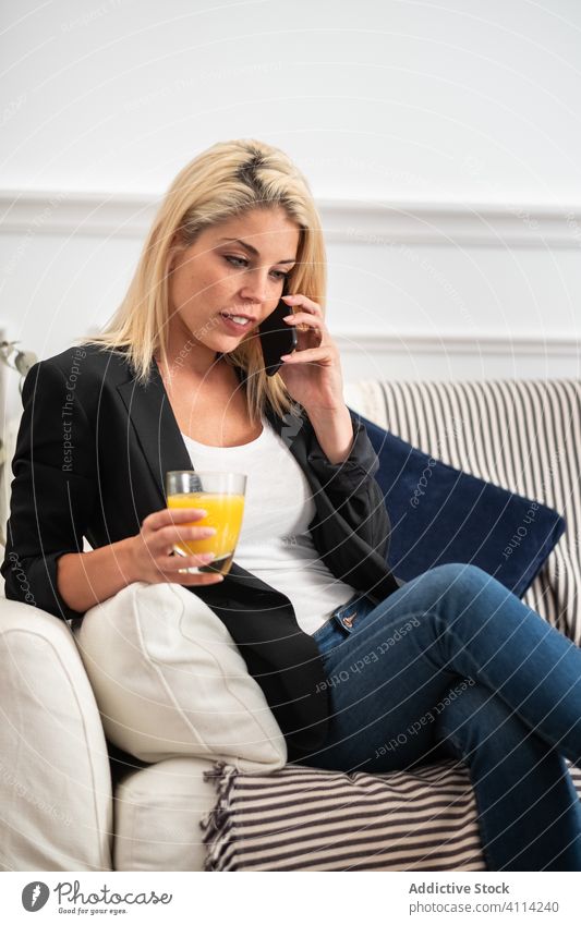 Frau trinkt Saft und benutzt Smartphone auf dem Sofa benutzend heimwärts Handy trinken ruhen soziale Netzwerke räkeln Gesundheit sitzen frisch orange Browsen