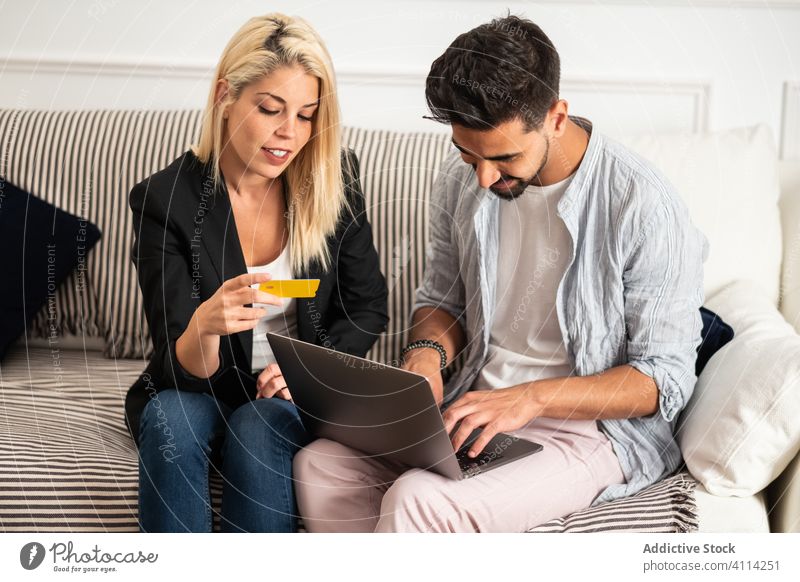 Glückliches buntes Paar beim Online-Shopping auf der Couch Werkstatt online Laptop Kreditkarte Zusammensein Sofa heimwärts Lächeln vielfältig Mann Frau