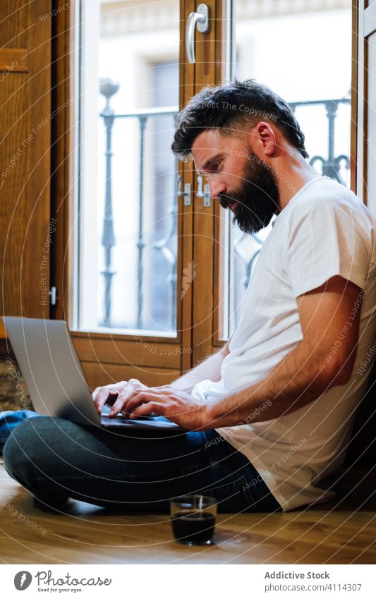 Bärtiger Freiberufler benutzt Laptop zu Hause Mann freiberuflich benutzend heimwärts Tippen trinken Stock Projekt modern männlich lässig Gerät Arbeit Internet