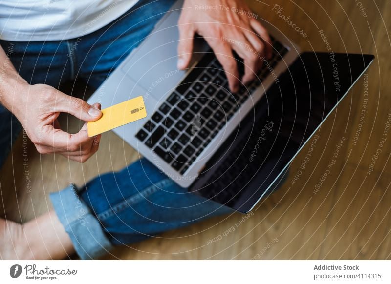 Crop Mann Einkaufen online auf dem Boden Kauf Laptop Kreditkarte benutzend sitzen Stock heimwärts Geld Werkstatt männlich Internet Gerät Browsen Apparatur