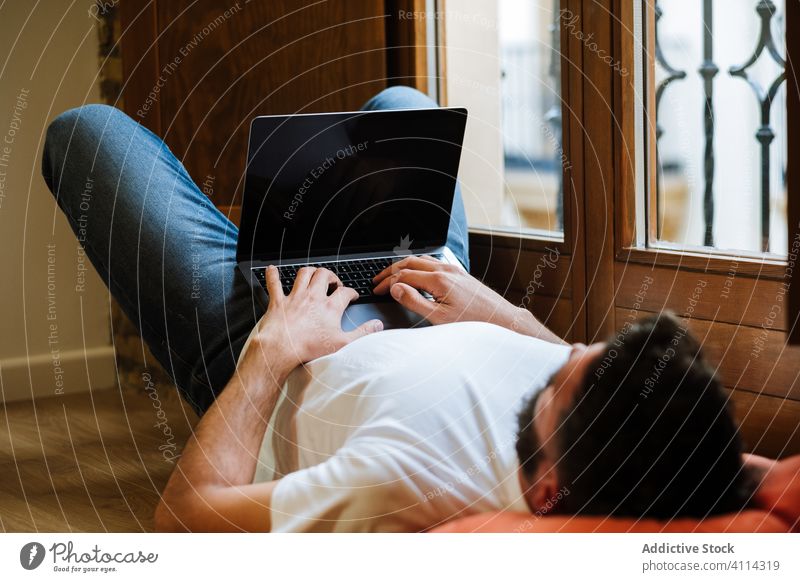 Freiberufler mit Laptop zu Hause Mann freiberuflich Lügen benutzend heimwärts Tippen trinken Stock Projekt modern männlich lässig Gerät Arbeit Internet