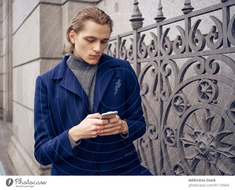 Stylischer junger Mann, der auf der Straße auf seinem Smartphone surft reden Großstadt Stil trendy elegant ernst besinnlich urban Metrosexualität Gerät