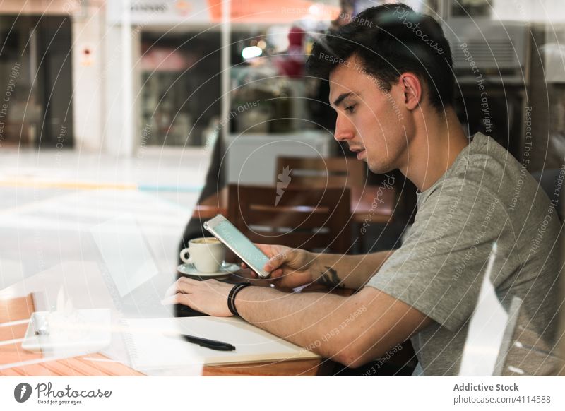 Männlicher Freiberufler mit Laptop und Smartphone in der Cafeteria Mann freiberuflich Café benutzend leerer Bildschirm Projekt Arbeit Tisch männlich Browsen