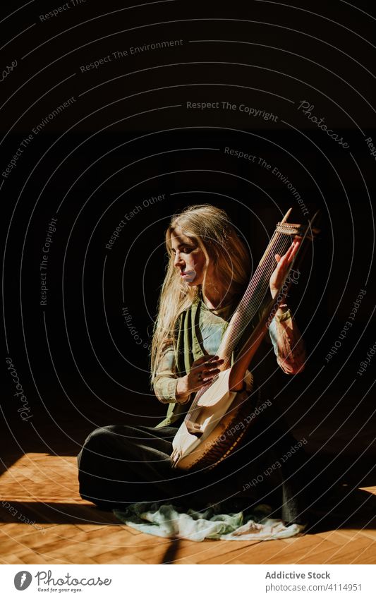 Dame spielt Leier in dunklem Raum Frau spielen lyra traditionell Musik heimwärts Stock dunkel sitzen blond tibetische Schale Melodie Erwachsener gemütlich Klang