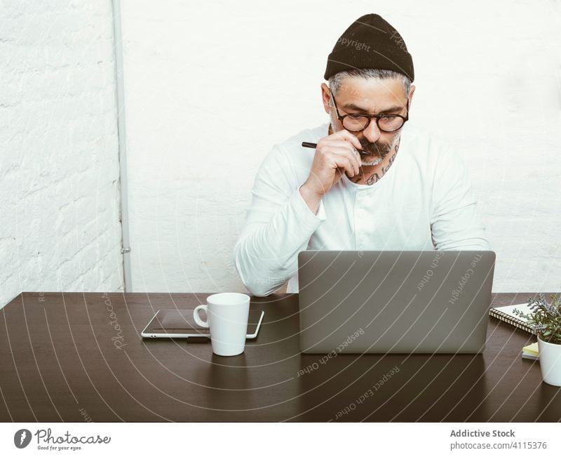 Erwachsener Mann arbeitet zu Hause am Laptop Arbeit freiberuflich benutzend Konzentration Quarantäne zur Kenntnis nehmen COVID19 Kopfbedeckung Brille männlich