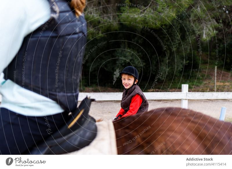 Kind und anonymer Teenager während einer Reitstunde Jockey Mitfahrgelegenheit Schule Dressur Arena Junge Mädchen Ponys Pferd Lektion Reiterin Pferderücken braun
