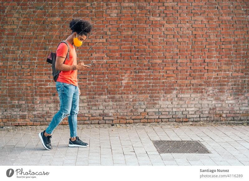 Afroamerikanischer Junge gehend laufen Spaziergang Seitenansicht Afro-Look jung Mann Gesichtsmaske Maske tragen schwarz Afroamerikaner urban außerhalb Lifestyle